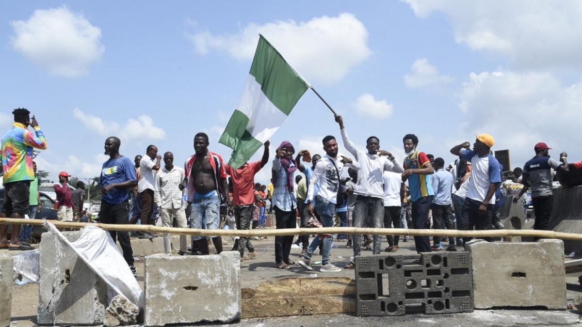 A protester raise the Nigerian national flag at a barricade mounted by potesters on the Lagos-Ibadan expressway to protest against police brutality and the killing of protesters by the military, at Magboro, Ogun State, on October 21, 2020. Buildings in Nigeria's main city of Lagos were torched on October 21, 2020 and sporadic clashes erupted after the shooting of peaceful protesters in which Amnesty International said security forces had killed several people. Witnesses said gunmen opened fire on a crowd of