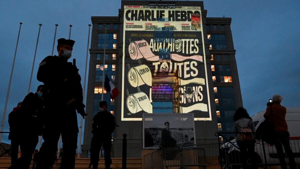 Police officers stand guard as cartoons of French satirical weekly newspaper Charlie Hebdo are projected onto the facade of the Hotel de Region in Montpellier, on October 21, 2020, during a national homage to French teacher Samuel Paty who was beheaded for showing cartoons of the Prophet Mohamed in his civics class. Pascal GUYOT / AFP