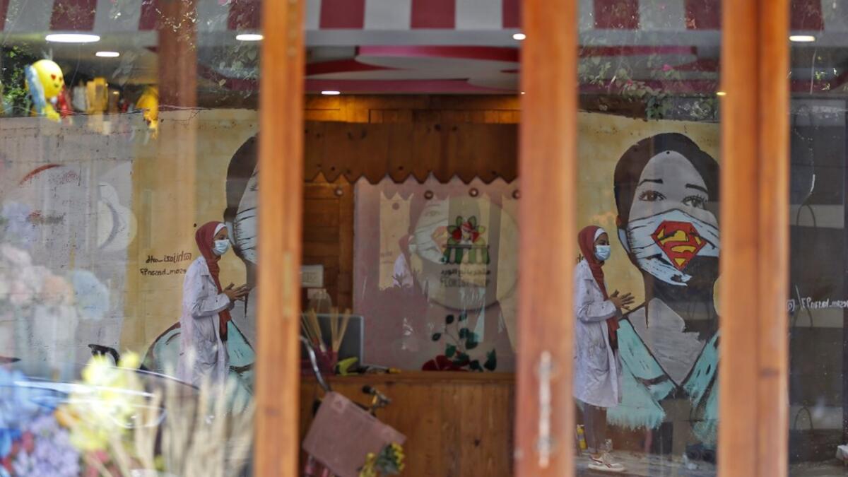 The image of a Palestinian student painting a large mural of a mask-clad girl is reflected on the doors of a shop in Gaza City on October 22, 2020, amid the novel coronavirus pandemic crises. Mohammed ABED / AFP