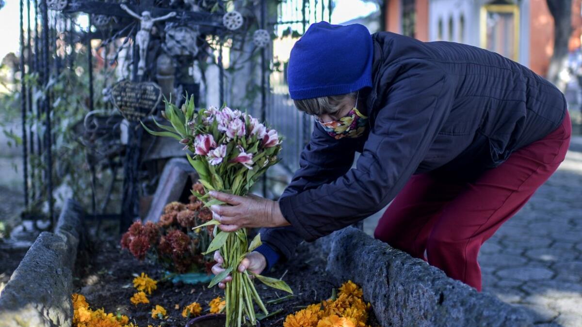 A woman decorates a relative's grave at La Magdalena Pantheon, in San Pedro Cholula, Puebla state, Mexico, on November 1, 2020, on All Saints' Day, amid the COVID-19 coronavirus pandemic. Local authorities have restricted the visit times and the number of visitors in cemeteries due to the pandemic. PEDRO PARDO / AFP