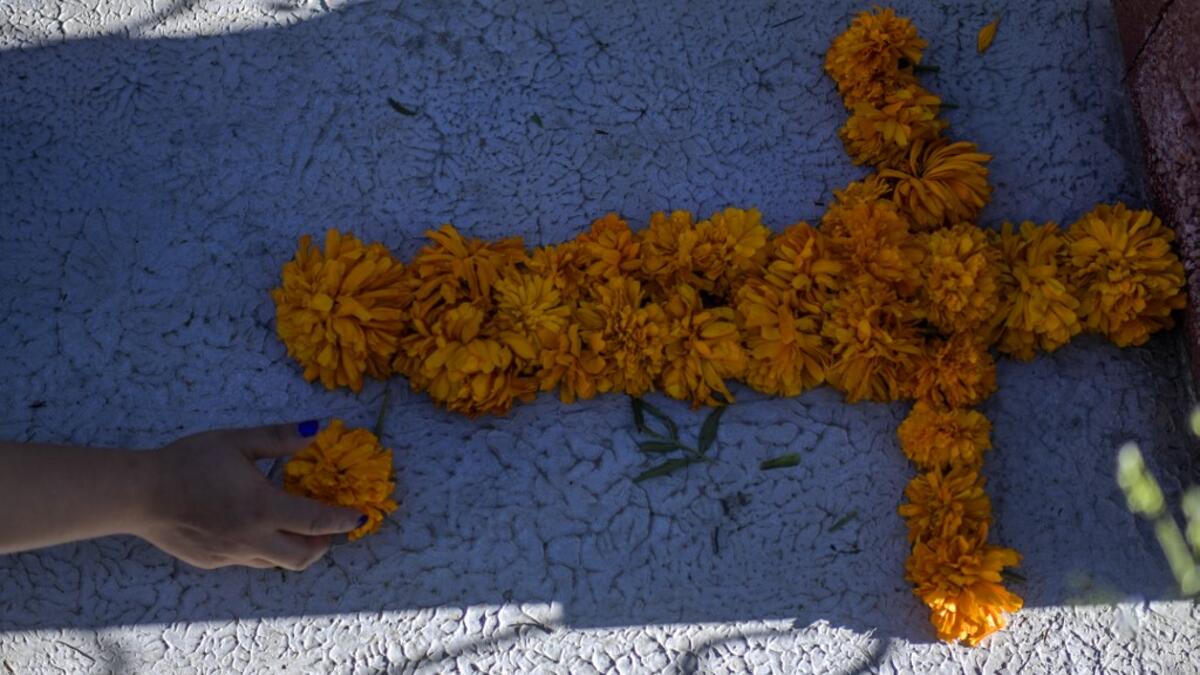 A woman decorates a relative's grave with Mexican marigolds forming a cross at La Magdalena Pantheon, in San Pedro Cholula, Puebla state, Mexico, on November 1, 2020, on All Saints' Day, amid the COVID-19 coronavirus pandemic. Local authorities have restricted the visit times and the number of visitors in cemeteries due to the pandemic. PEDRO PARDO / AFP