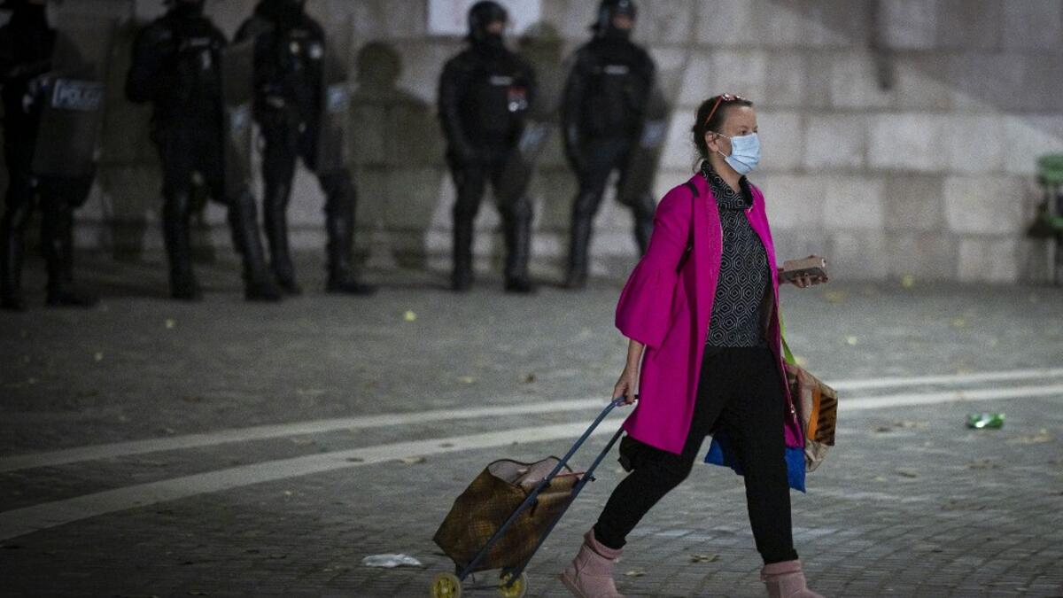 A woman with a shopping trolley walks past police officers wearing anti-riot gear as protesters clash with police during the rally against government’s coronavirus restrictions in Ljubljana on November 5, 2020. Jure Makovec / AFP