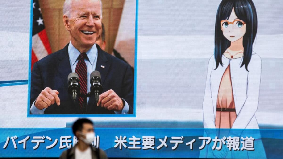 A man wearing a face mask walks in front of a huge screen showing a news programme featuring US Democratic candidate Joe Biden's win in the US presidential election, in Tokyo on November 8, 2020. Behrouz MEHRI / AFP