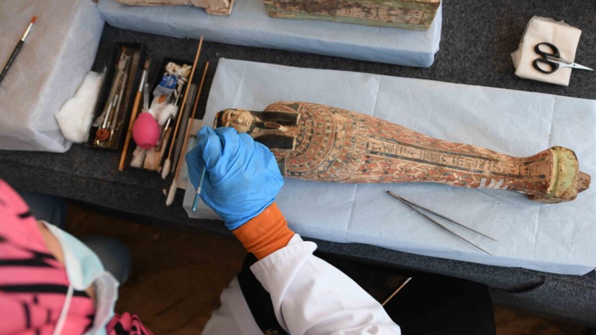 An archaeologist cleans a statue during the unveiling of an ancient treasure trove of more than a 100 intact sarcophagi, at the Saqqara necropolis 30 kms south of the Egyptian capital Cairo, on November 14, 2020. Egypt announced the discovery of an ancient treasure trove of more than a 100 intact sarcophagi, the largest such find this year. The sealed wooden coffins, unveiled on site amid fanfare, belonged to top officials of the Late Period and the Ptolemaic period of ancient Egypt. They were found in thre