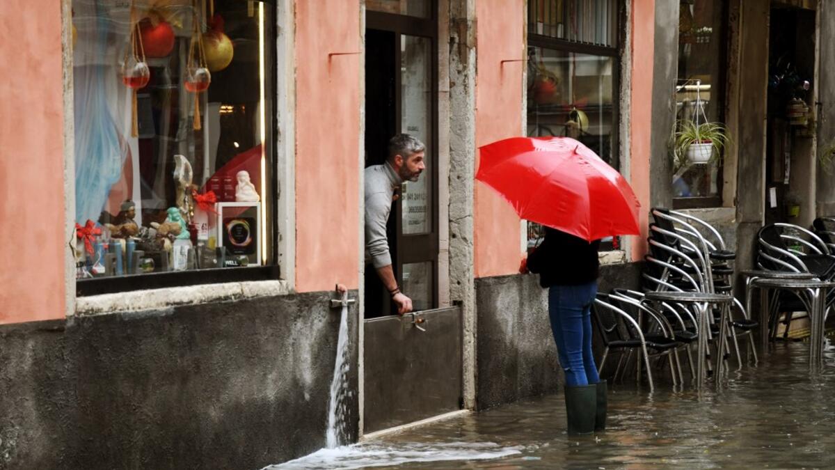 A shop owner protects water from getting in on December 8, 2020 in Venice following a high tide "Alta Acqua" event following heavy rains and strong winds, and the mobile gates of the MOSE Experimental Electromechanical Module that protects the city of Venice from floods, were not lifted ANDREA PATTARO / AFP