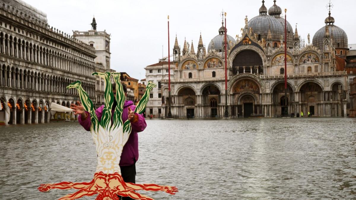 A view shows a flooded St. Mark's Square as a man poses for a photo by a cardboard cutout of the Vitruvian Man, on December 8, 2020 following a high tide "Alta Acqua" event following heavy rains and strong winds, and the mobile gates of the MOSE Experimental Electromechanical Module that protects the city of Venice from floods, were not lifted. ANDREA PATTARO / AFP