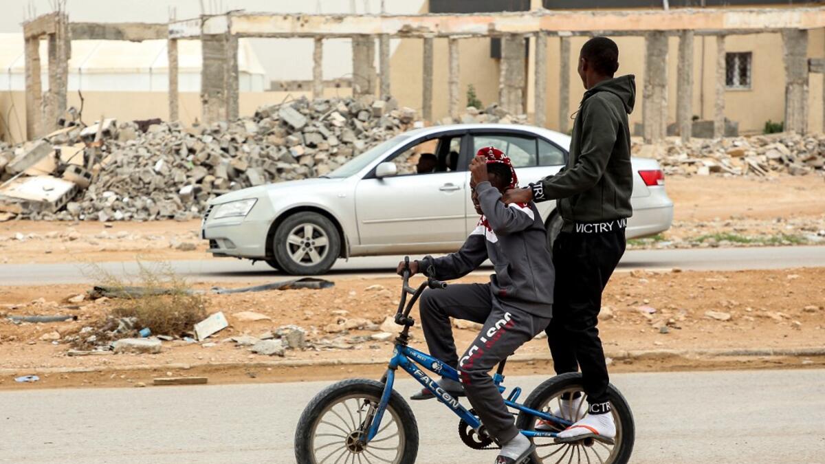 A boy rides behind another on a bicycle along a road past destroyed buildings in the city of Tawergha, some 200 kilometres (125 miles) east of Libya's capital close to the port city of Misrata, on December 12, 2020. When Libyan dictator Moamer Kadhafi was toppled, people took revenge on those they saw as his supporters -- including the entire town of Tawergha, whose 40,000 residents were forced to flee. Now, almost a decade later since militia forces rampaged through the town torching homes, destroying buil