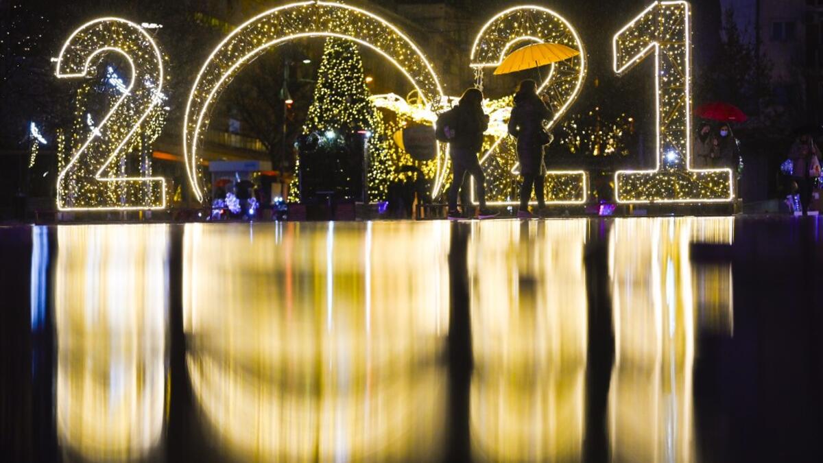 Women walk under an umbrella in front of a 2021 sign displayed in downtown Pristina on December 30, 2020, as Kosovars prepare to celebrate the New Year 2021 at their homes, amid the ongoing Covid-19 (novel coronavirus) pandemic. Armend NIMANI / AFP
