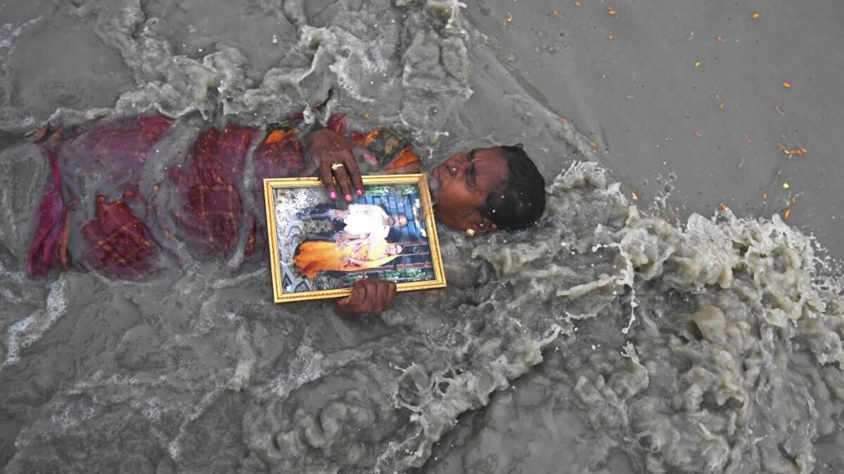 A Hindu pilgrim holds a picture of herself with late husband as she takes a holy dip at the confluence of Ganges and the Bay of Bengal during the Gangasagar Mela on the occasion of Makar Sankranti, a day considered to be of great religious significance in Hindu mythology, at Sagar Island, around 150 kms south of Kolkata on January 14, 2021. Dibyangshu SARKAR / AFP