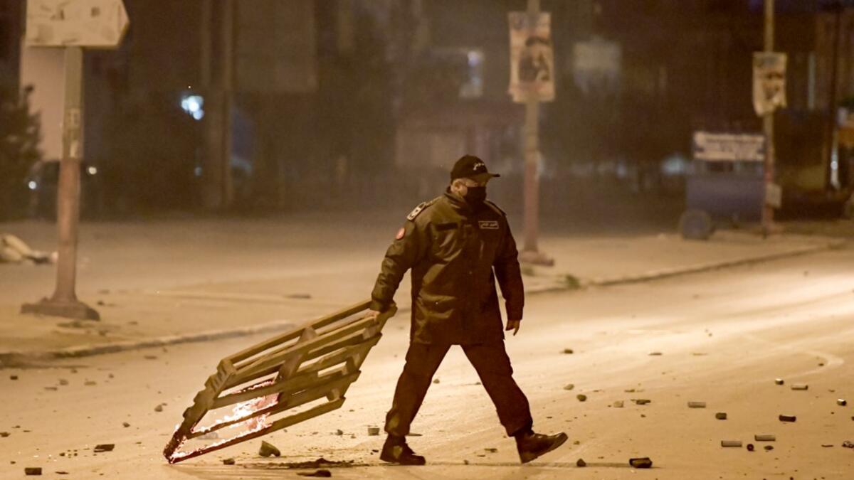A member of Tunisia's National Guard drags a burning wooden mesh during clashes with protesters in the Ettadhamen city suburb on the northwestwern outskirts of Tunisia's capital Tunis on January 17, 2021, amidst a wave of nightly protests in the North African country. FETHI BELAID / AFP