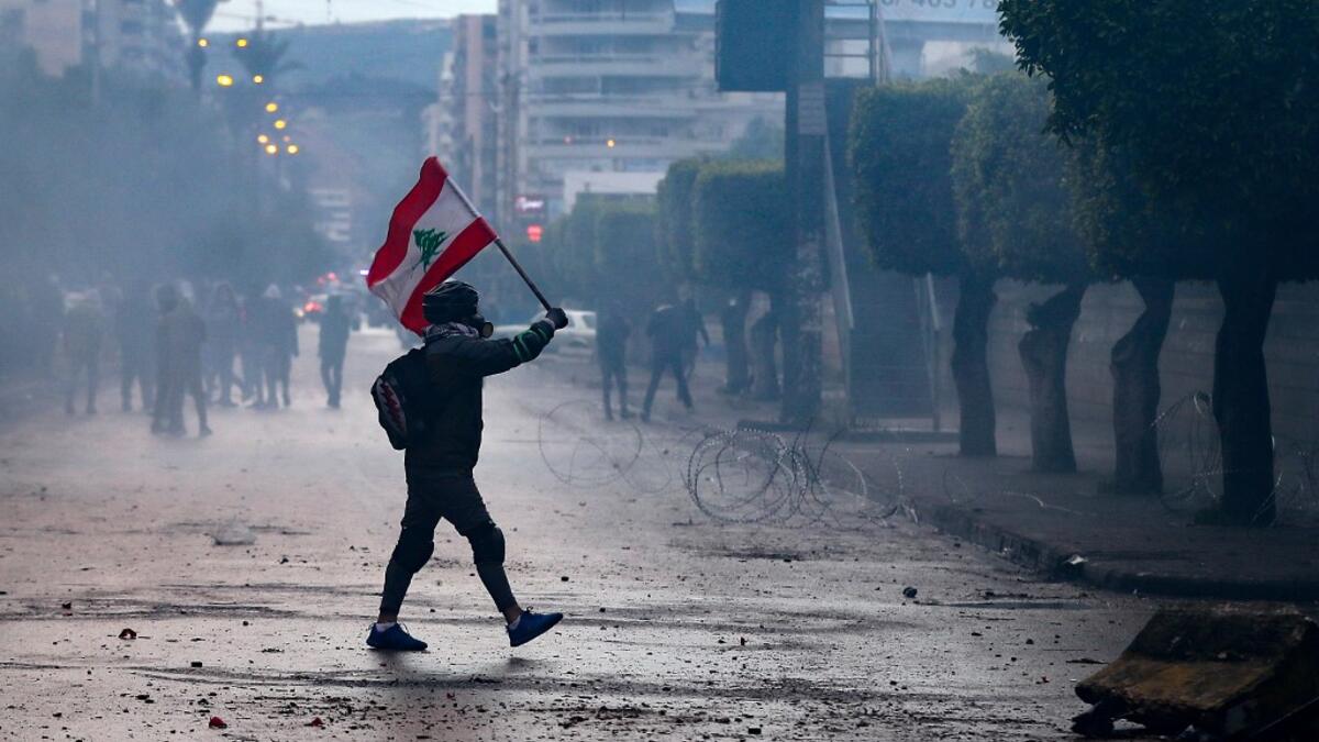 A Lebanese anti-government protester waves a national flag during clashes with security forces in front of the Serail (headquarters of the Governorate), in the northern port city of Tripoli, following a demonstration to protest against the economic situation, on January 28, 2021. Tripoli was already one of Lebanon's poorest areas before the coronavirus pandemic piled new misery onto a chronic economic crisis. Many of its residents have been left without an income since Lebanon imposed a full lockdown earlie