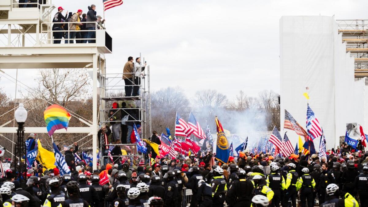 Pro-Trump protesters stand on a media platform in front of a line of police officers after breaking through barriers onto the grounds of the Capitol Building on January 6, 2021 in Washington, DC. A pro-Trump mob stormed the Capitol earlier, breaking windows and clashing with police officers. Trump supporters gathered in the nation's capital to protest the ratification of President-elect Joe Biden's Electoral College victory over President Donald Trump in the 2020 election. Jon Cherry/Getty Images/AFP