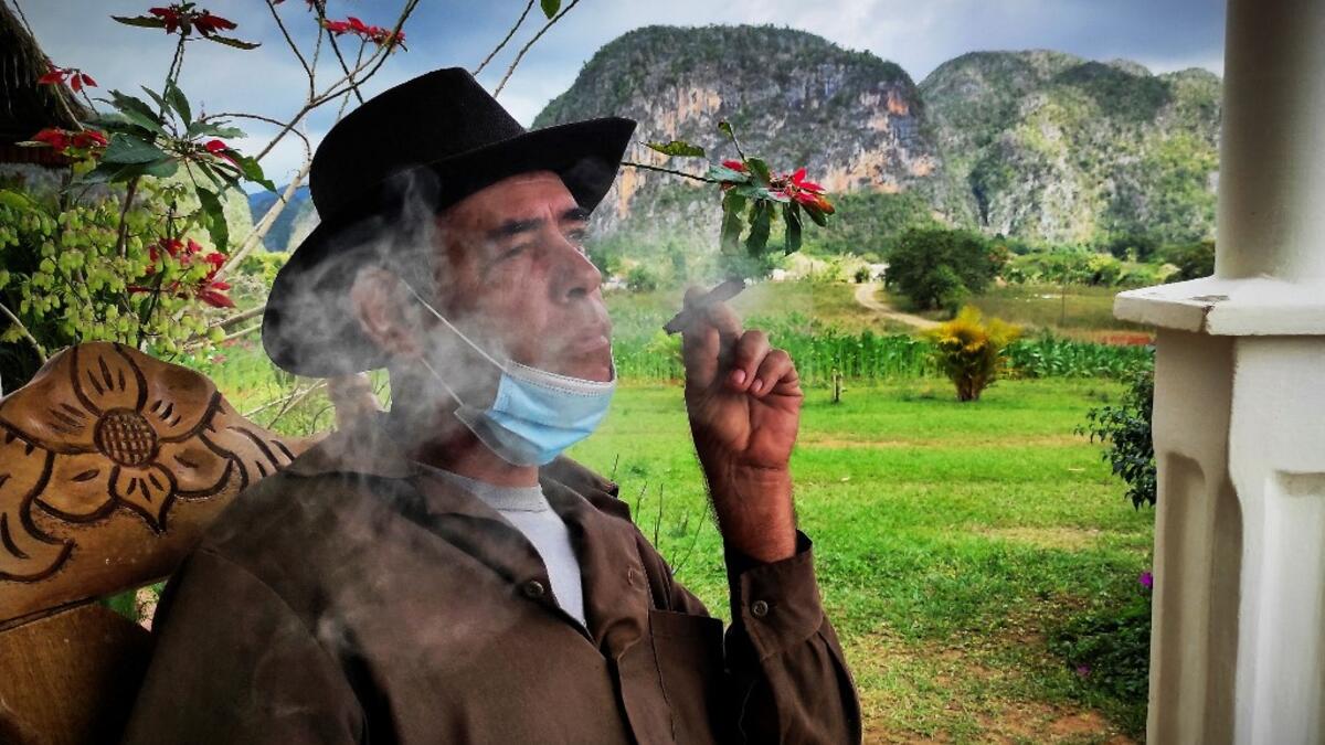 Eduardo Hernandez, owner of a private restaurant and a tobacco cultivator, smokes a cigar in his house in Vinales, Cuba, on January 28, 2021. At the foot of the majestic rock formations of Vinales, the terraces of the restaurants look empty and the lodgings have closed. With the arrival of COVID-19, the incipient prosperity of this Cuban town came to a halt and people abandoned tourism jobs to return to work the land. YAMIL LAGE / AFP