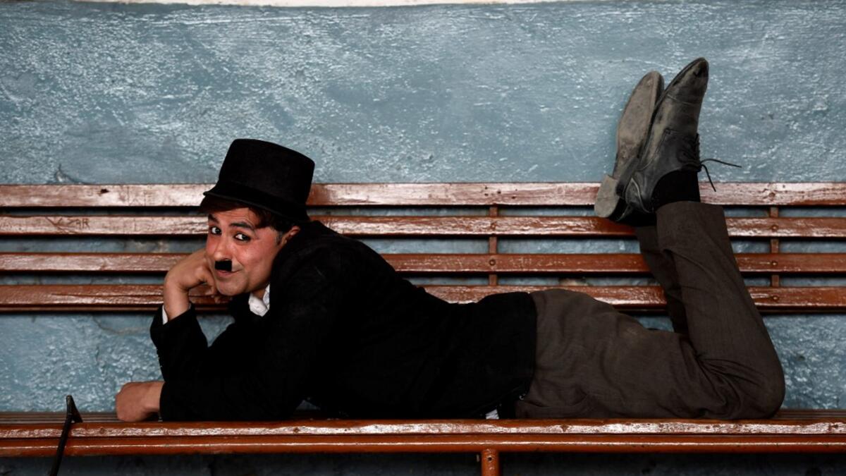 In this picture taken on February 9, 2021, street actor Usman Khan, dressed up as silent film star Charlie Chaplin, performs at a train station in the Pakistan's northwestern city of Peshawar. Wearing a bowler hat and familiar toothbrush moustache, Pakistan's Usman Khan darts through traffic swinging a cane, teasing motorists and shopkeepers for laughs and a few rupees with a Charlie Chaplin impersonation that has become a viral sensation.  Abdul MAJEED / AFP