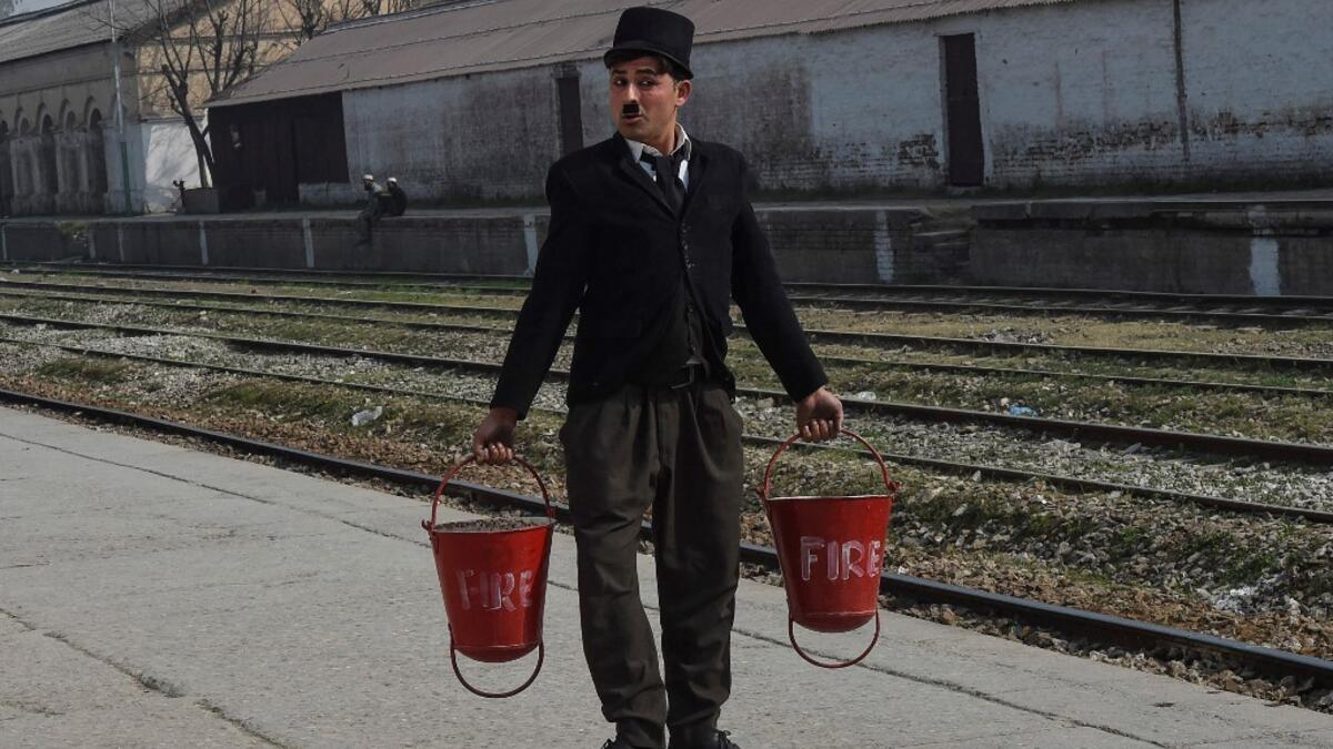 In this picture taken on February 9, 2021, street actor Usman Khan, dressed up as silent film star Charlie Chaplin, performs at a train station in the Pakistan's northwestern city of Peshawar. Wearing a bowler hat and familiar toothbrush moustache, Pakistan's Usman Khan darts through traffic swinging a cane, teasing motorists and shopkeepers for laughs and a few rupees with a Charlie Chaplin impersonation that has become a viral sensation.  Abdul MAJEED / AFP