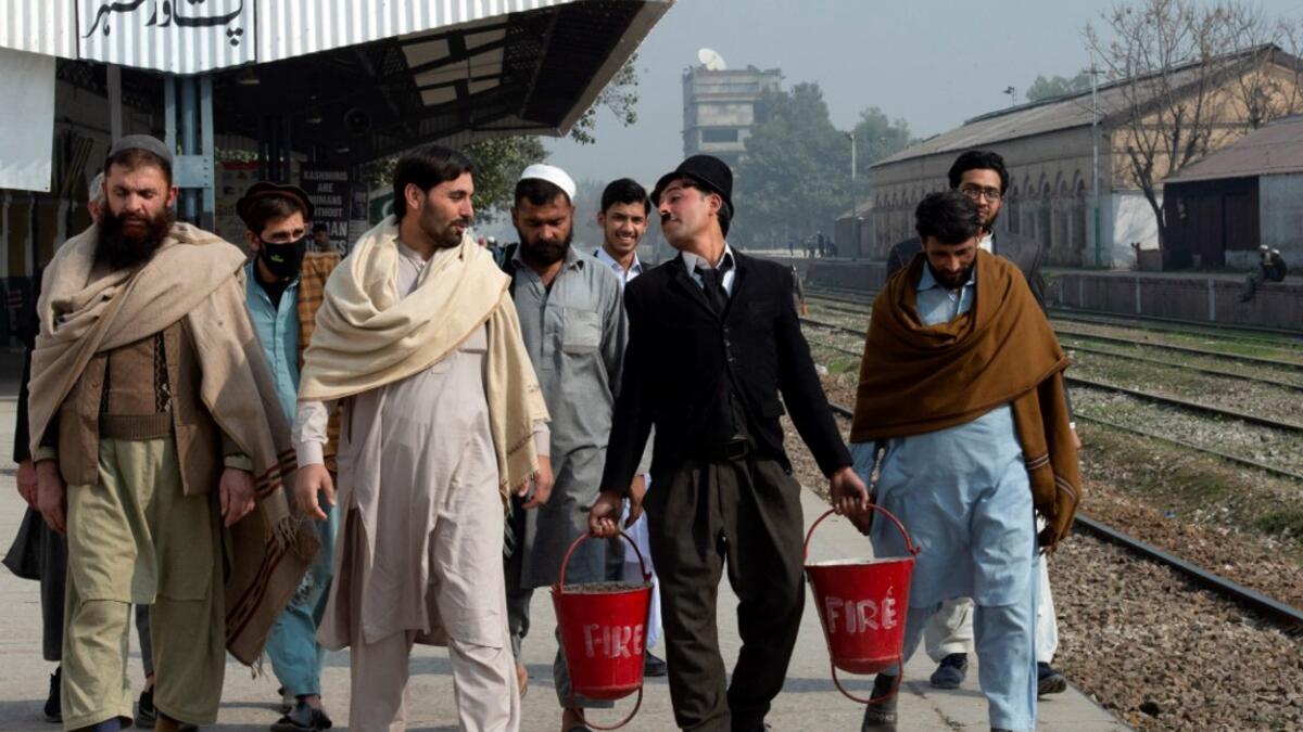 In this picture taken on February 9, 2021, street actor Usman Khan (2nd R), dressed up as silent film star Charlie Chaplin, performs at a train station in the Pakistan's northwestern city of Peshawar. Wearing a bowler hat and familiar toothbrush moustache, Pakistan's Usman Khan darts through traffic swinging a cane, teasing motorists and shopkeepers for laughs and a few rupees with a Charlie Chaplin impersonation that has become a viral sensation.  Abdul MAJEED / AFP