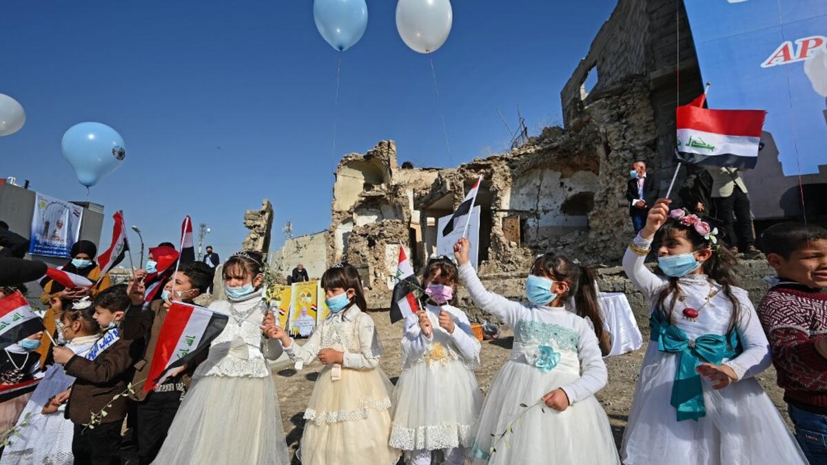 Iraqi children dressed in costumes wave national flags near the ruins of the Syriac Catholic Church
