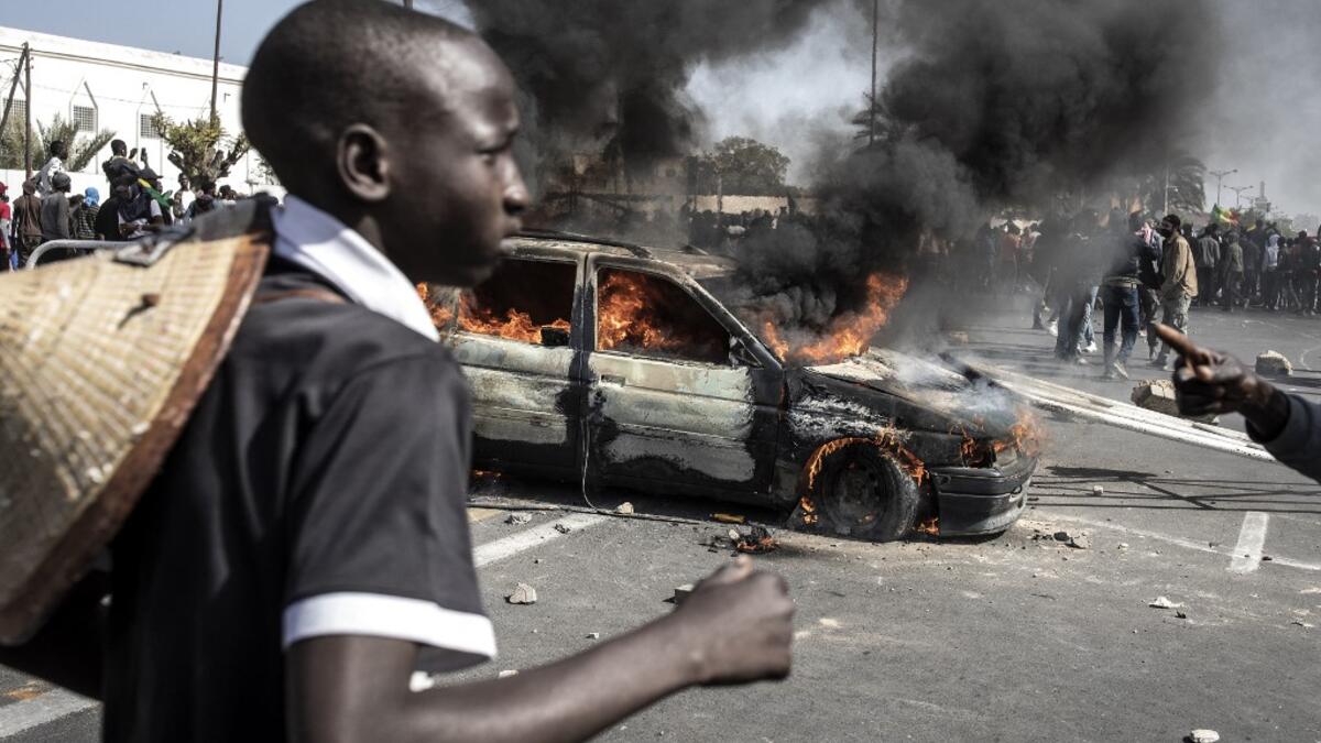 A protester runs past a burning car during a protest in Dakar on March 8, 2021, after the country's opposition leader Ousmane Sonko was charged with rape. Usually considered a beacon of stability in a volatile region, deadly clashes between opposition supporters and security forces have rocked the West African state. JOHN WESSELS / AFP