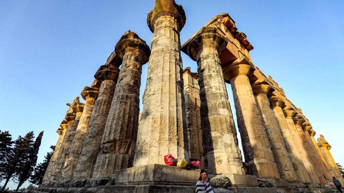 A costumed actress sits by a column during the filming of a television production at the Temple of Zeus in the ruins of Libya
