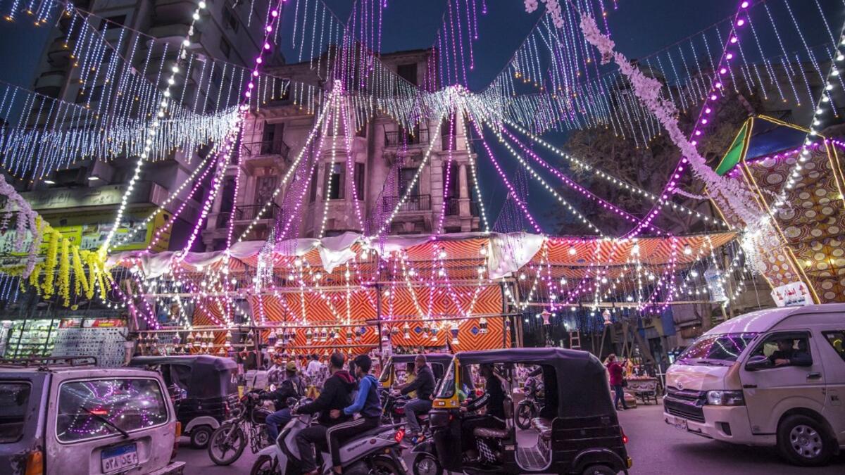 Vehicles, motorcycles, and tuk-tuks (motorised rickshaws) drive past a stall selling Ramadan lanterns