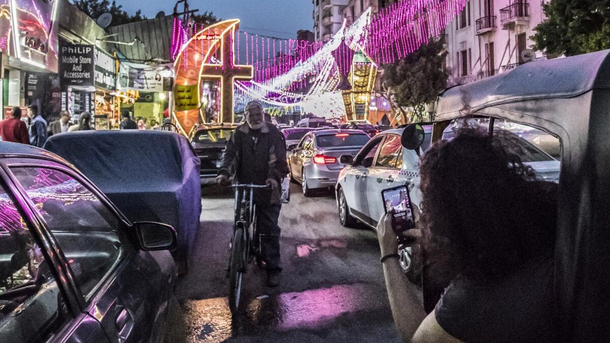 A woman riding in a tuk-tuk (motorised rickshaw) peeks out to use her phone to photograph a man riding a bicycle