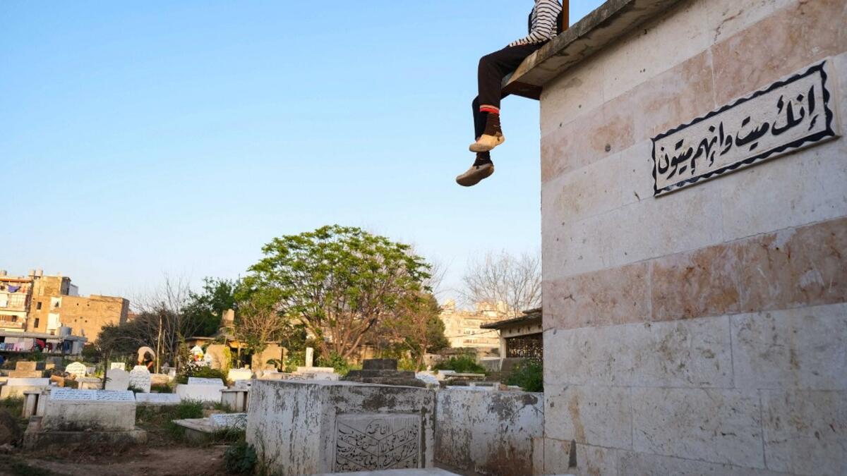 A boy sits atop a grave with a sign quoting the Holy Koran