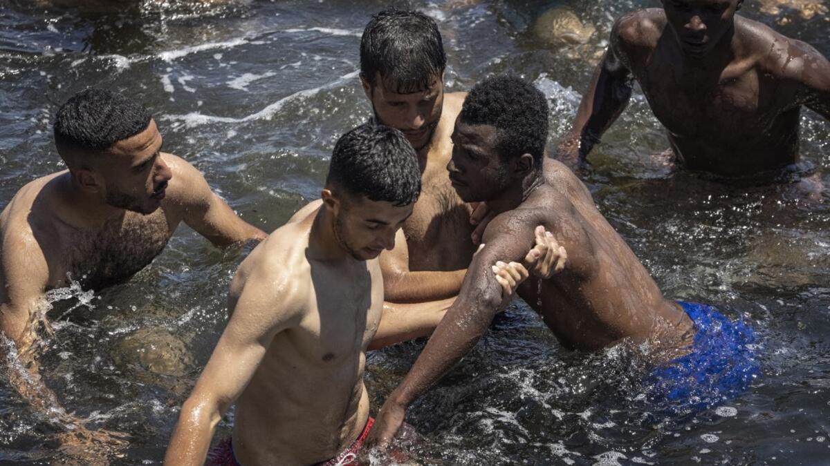 Moroccan migrants save a subsaharian migrant who had difficulty in the water as he attemped to swim from the northern town of Fnideq across the border from Morocco to Spain's North African enclave of Ceuta on May 19, 2021. Spain stepped up diplomatic pressure on Rabat as its prime minister flew into Ceuta, vowing to "restore order" in the North African enclave after a record 8,000 migrants reached its beaches from Morocco