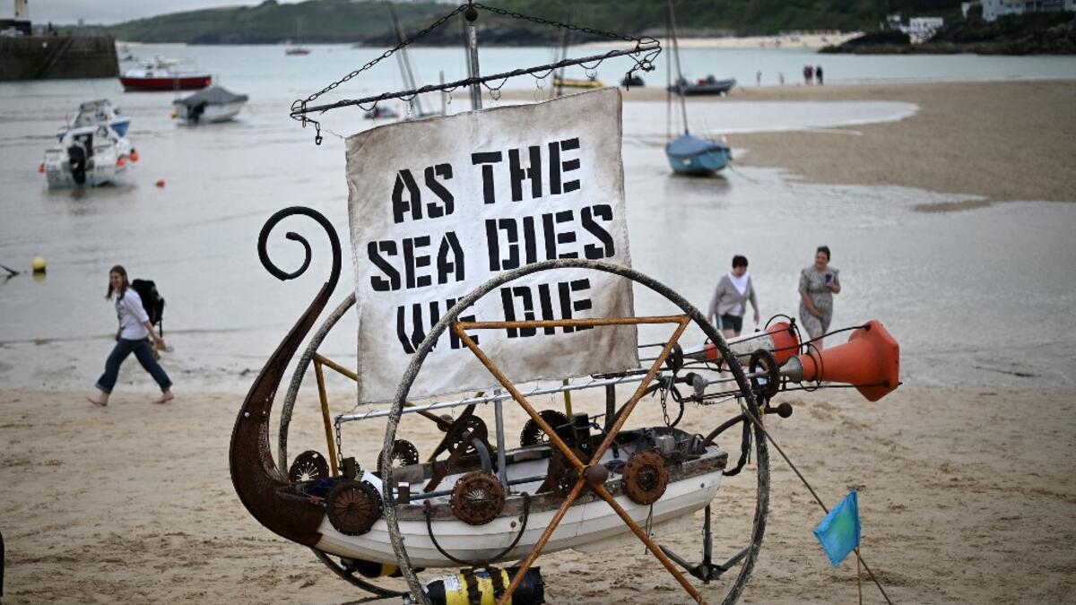 A boat sculpture with the words 'As the sea dies, we die' written on the sail is pictured during an Extinction Rebellion climate change protest on the beach in St Ives, Cornwall on June 11, 2021, on the first day of the three-day G7 summit being held from 11-13 June. G7 leaders from Canada, France, Germany, Italy, Japan, the UK and the United States meet this weekend for the first time in nearly two years, for the three-day talks in Carbis Bay,