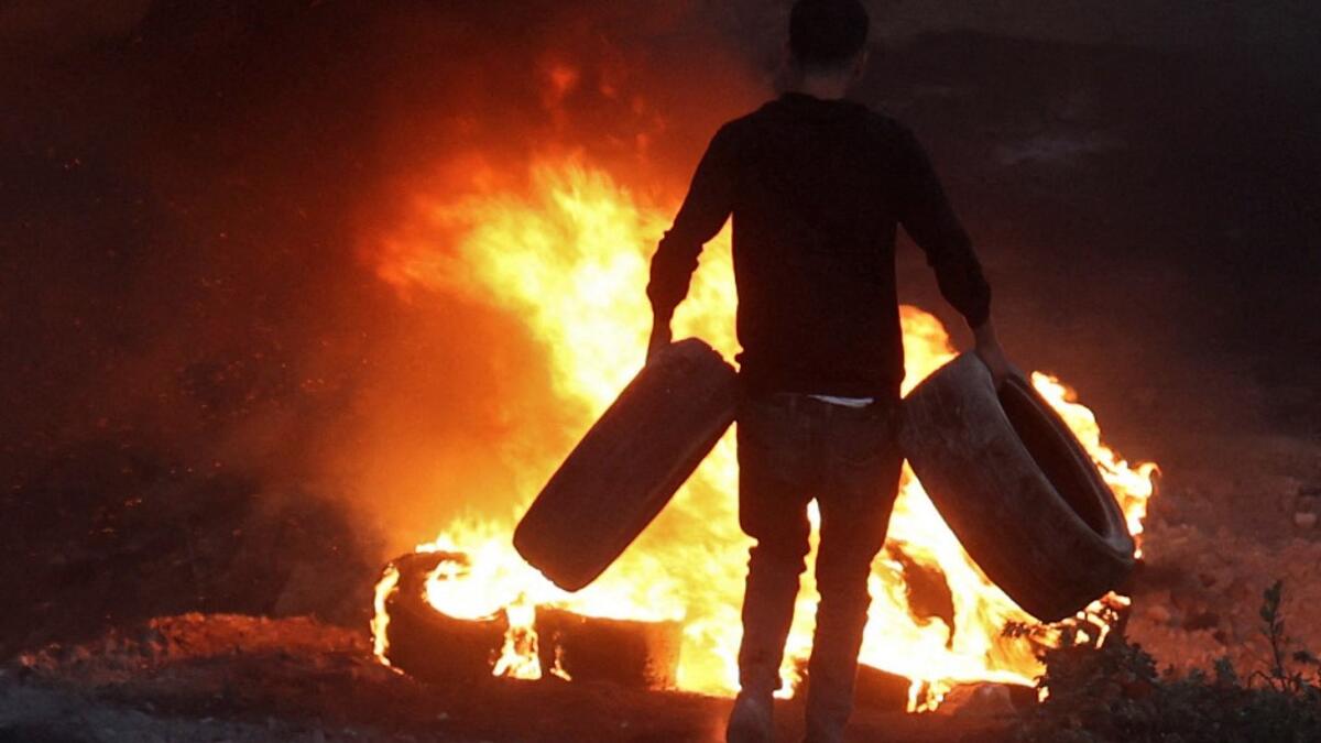 A Palestinian man sets a tire on fire in the village of Beita, south of Nablus, in the occupied West Bank, across the valley from the newly built Israeli settlers' outpost of Eviatar, on June 13, 2021. With flashing lasers, honking horns and choking smoke from burning tires, the latest tactics used by Palestinian protesters are dusk till dawn rallies to make life unbearable for Israeli settlers.