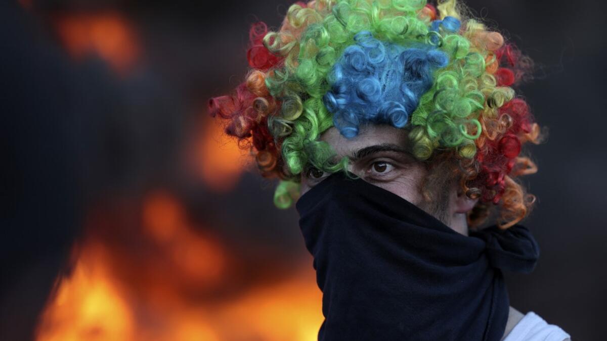 A man wears a face cover and a colorful wig as Palestinians burn tires during a night demonstration the expansion of the Jewish settlement outpost of Eviatar on the lands of Beita village, near the occupied West Bank city of Nablus
