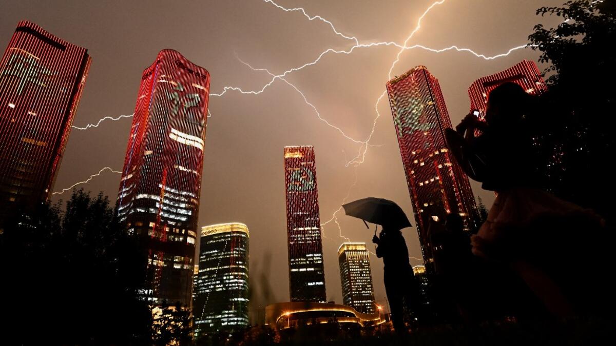 A bolt of lightning crosses the sky as people look at buildings displaying a light show on the eve of the 100th anniversary of the Chinese Communist Party in Beijing