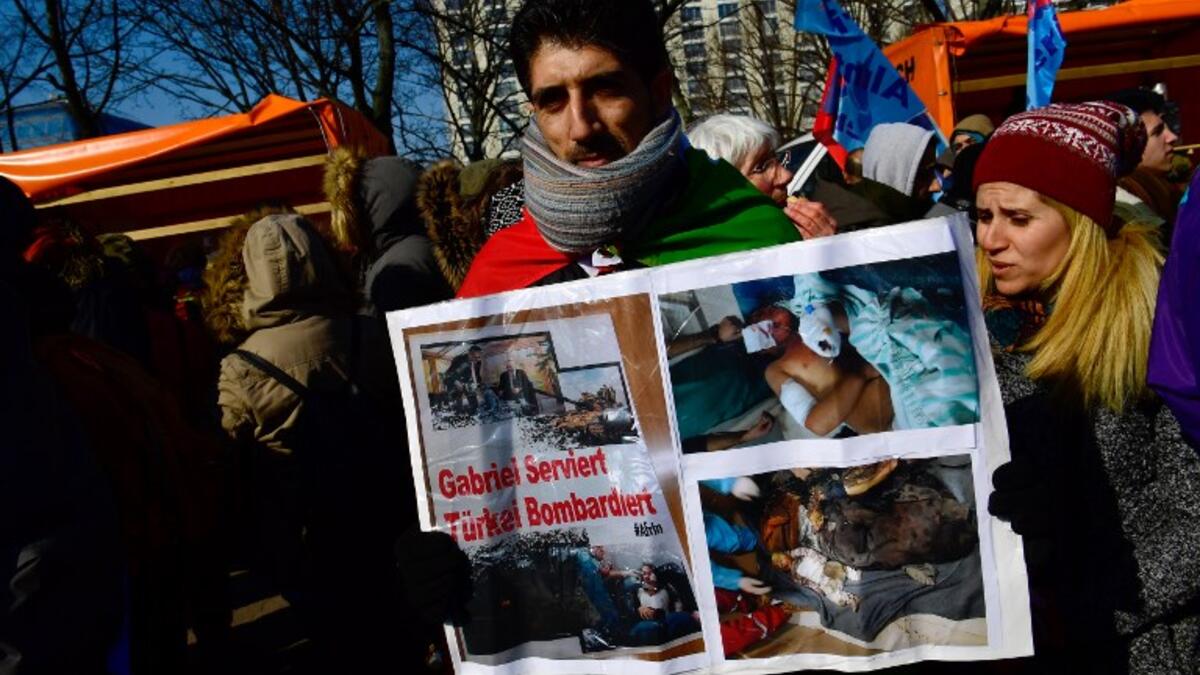 A protester holds a poster depicting injured people and showing a photograph (top L) of German Foreign Minister Sigmar Gabriel serving his Turkish counterpart Mevlut Cavusoglu during the demonstration; text reads "Gabriel serves, Turkey bombs". (JOHN MACDOUGALL / AFP)