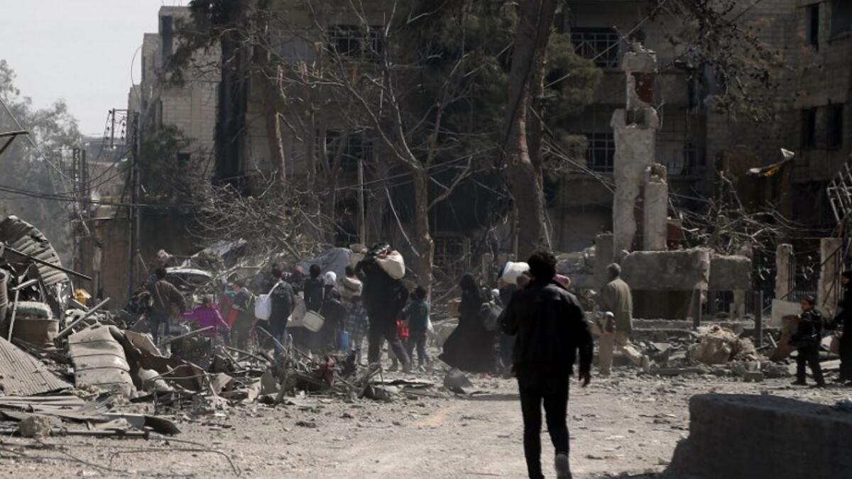 People carry their belongings as they flee their homes in the town of Hamouria in Syria's eastern Ghouta region on Mar. 15, 2018. (ABDULMONAM EASSA / AFP)