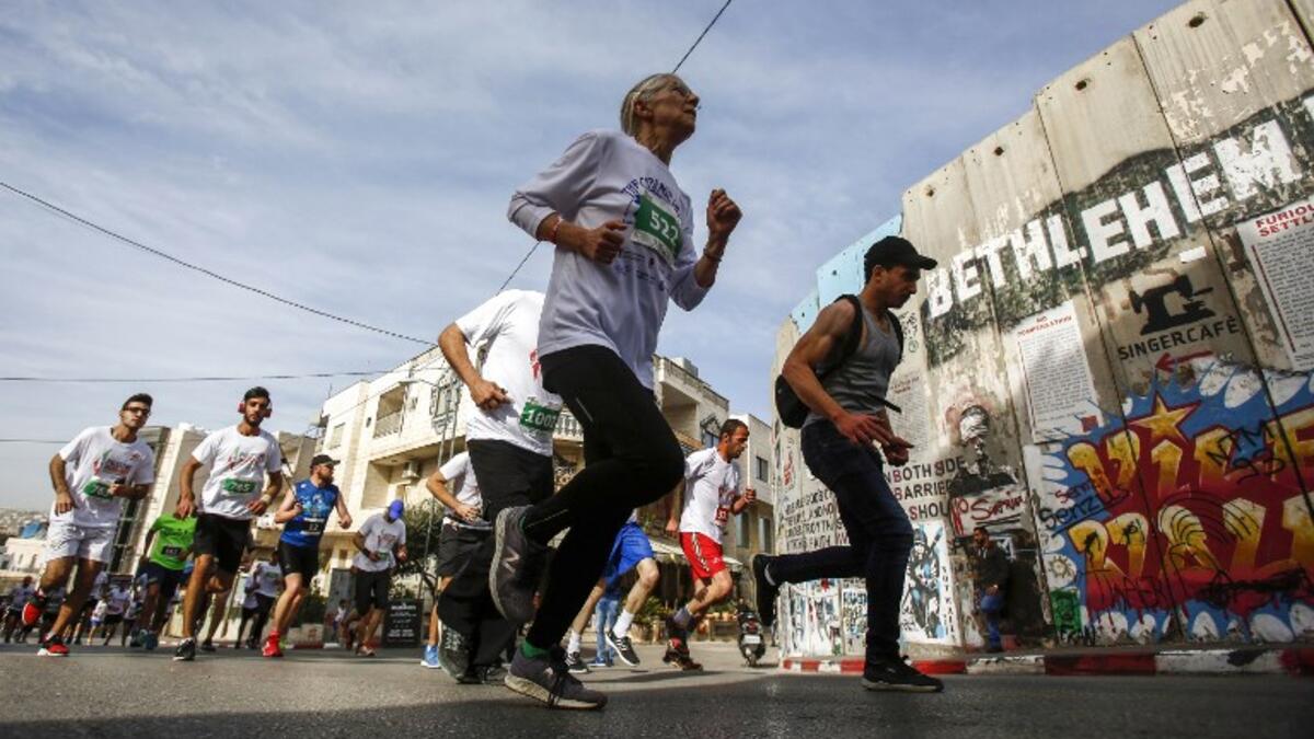 Participants run past Banksy's "The Walled-Off Hotel" near Israel's controversial separation barrier, which divides the West Bank from Jerusalem, in the biblical town of Bethlehem during the 6th International Palestine Marathon on Mar. 23, 2018. 
(Musa AL SHAER / AFP)