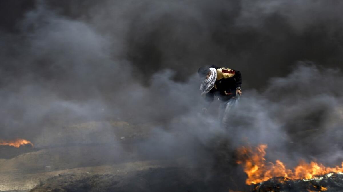 A Palestinian protester runs for cover amidst the fumes from burning tires during clashes with Israeli forces across the border, following a demonstration calling for the right to return.
(MOHAMMED ABED / AFP)