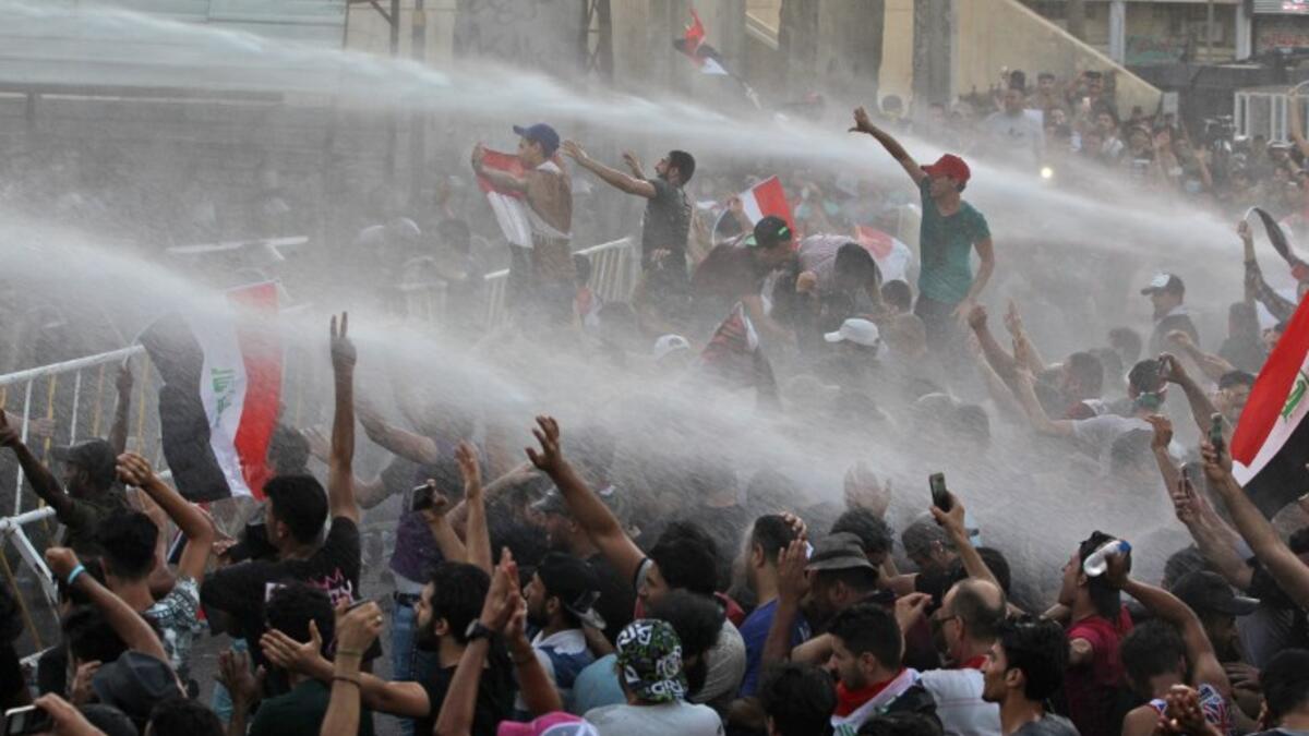 Iraqi protesters waving national flags are being sprayed with water cannon by security forces during a demonstration against unemployment and a lack of basic services in the capital Baghdad's Tahrir Square on July 20, 2018. (AFP/ Ahmad Al Rubaye)