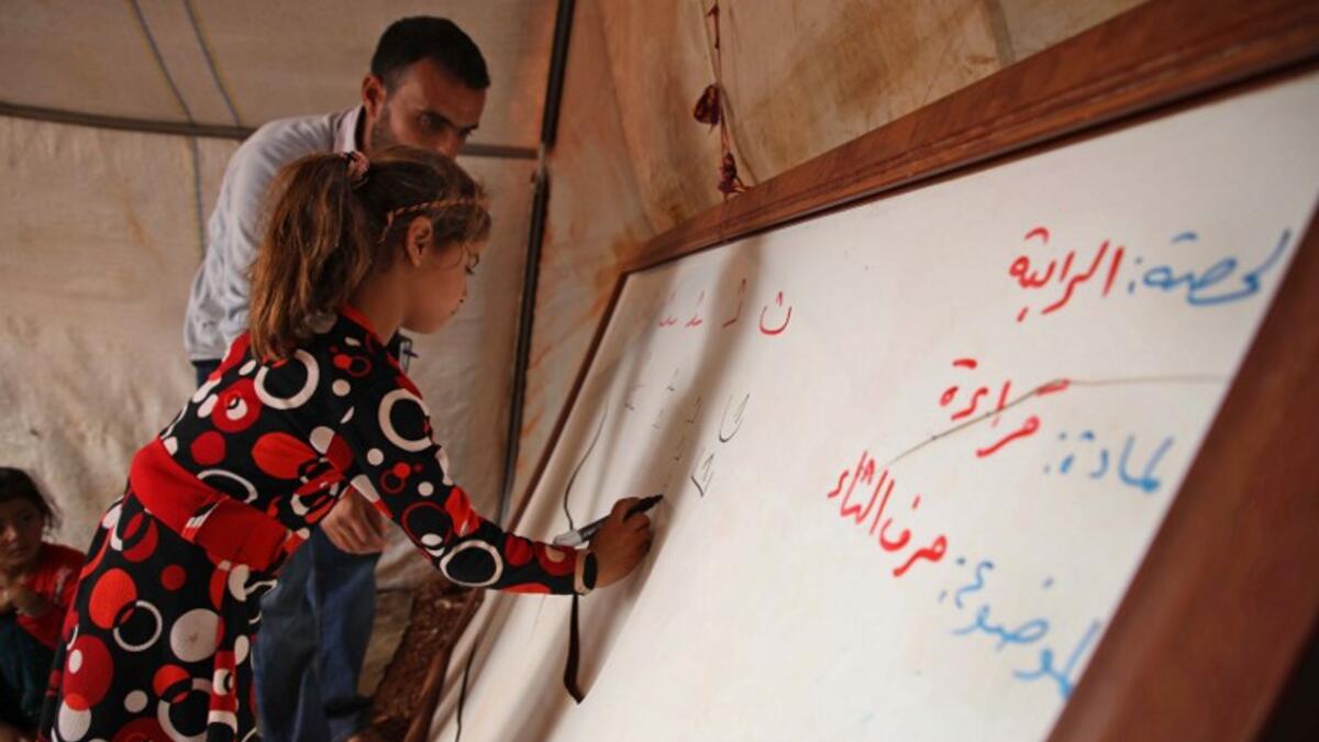 A Syrian child who fled with her family from the northern countryside of Hama, writes on the borad in a classoom at the makeshift school of "Zuhur al-Mustaqbal" Aaref WATAD / AFP