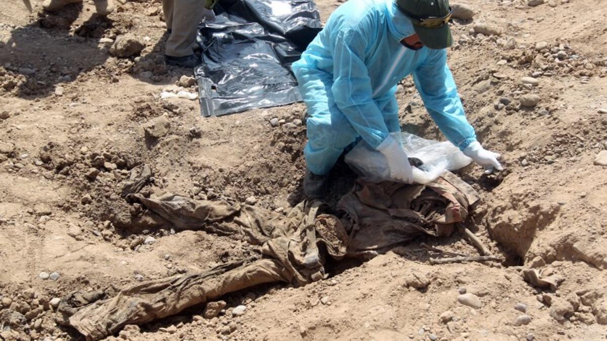 A member of the Iraqi security forces wearing protective clothes inspects a mass grave containing the remains of dozens of people killed by ISIS. (Ahmad AL-RUBAYE / AFP)