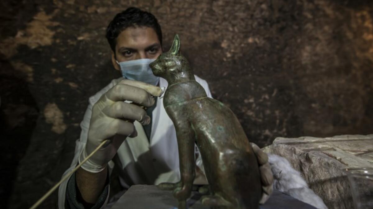 An Egyptian archaeologist cleans a bronze ancient Egyptian sitting cat statue, on November 10, 2018. (KHALED DESOUKI / AFP)