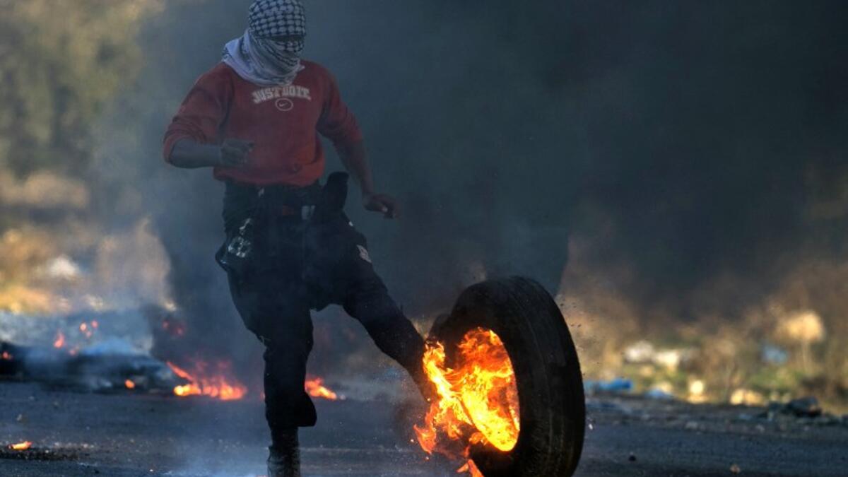 A Palestinian protester kicks a burning tire towards Israeli security forces during clashes in the West Bank city of Nablus, following a demonstration against US President Donald Trump's decision to recognize Jerusalem as the capital of Israel on Dec. 9, 2017. 
(JAAFAR ASHTIYEH / AFP)