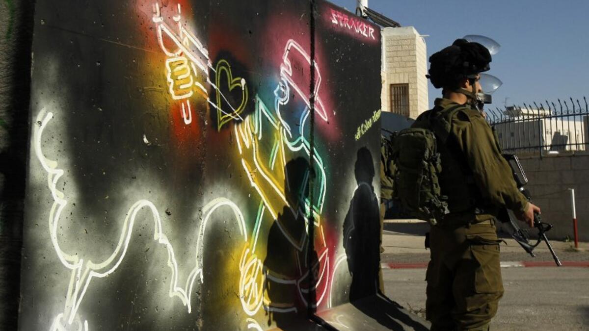 Israeli forces stand guard in front of a mural at the main entrance of Bethlehem, in the Israeli occupied West Bank as protests continue in the region.
(Musa AL SHAER / AFP)