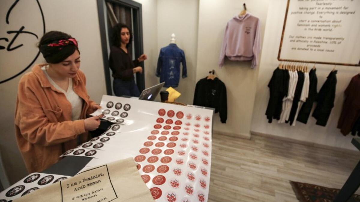 Amira Khader (L), Palestinian creative director of the feminist fashion label "BabyFist", cuts stickers while founder Yasmeen Mjalli stands next to her in their shop in Ramallah 
ABBAS MOMANI / AFP