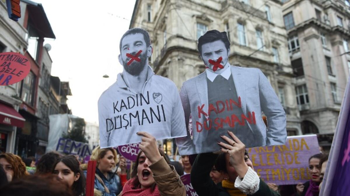A women's rights activist holds a picture of Turkish football player Arda Turan (L) with the lettering 'Enemy of woman' as activists march through Taksim Square to protest against gender violence in Istanbul, on November 25, 2018, on the International Day for the Elimination of Violence against Women. 
BULENT KILIC / AFP