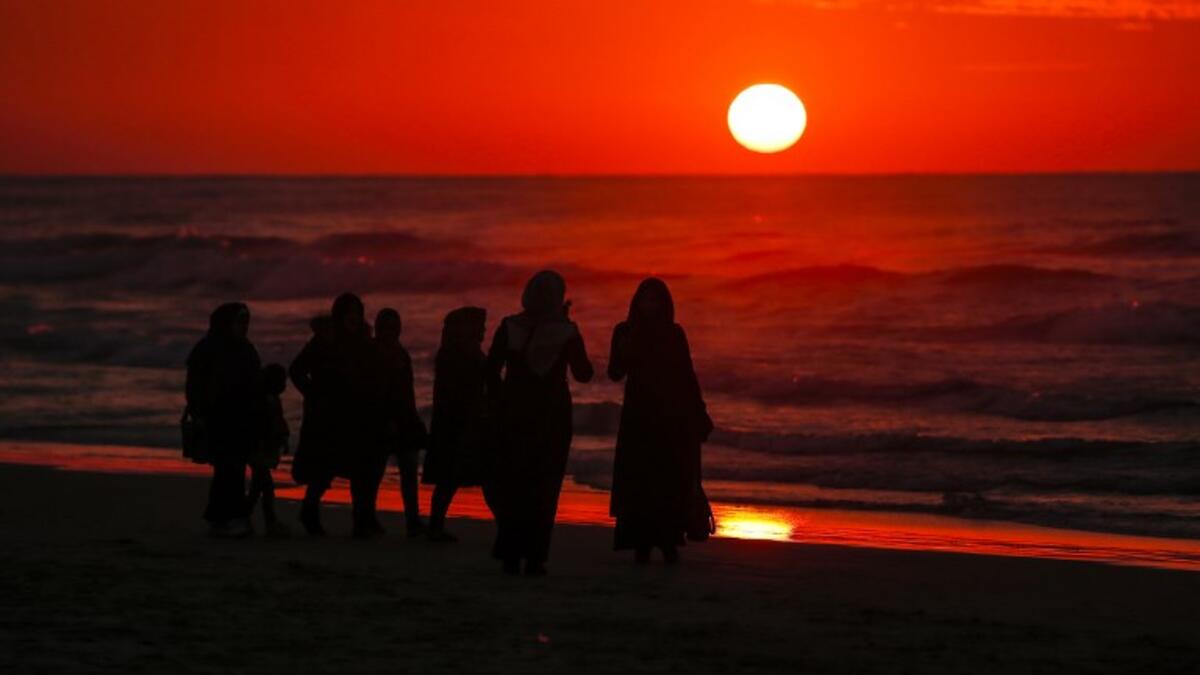 Palestinian people walk on the beach at sunset a few hours prior to the new year's celebrations, west of in Gaza city on December 31, 2018. 
MAHMUD HAMS / AFP