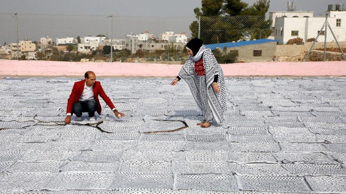 Palestinian Southern Education Direction's member Safa'a Amro (R) prepares a one thousand four hundred Meter square Keffiyeh. (HAZEM BADER / AFP)