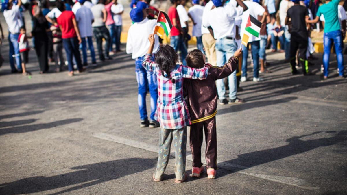 A brother and sister wave flags and watch as planes from the Royal Jordanian Air Force fly overhead in the air show.