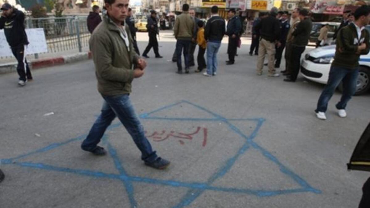A Palestinian youth walks on a Star of David sprayed on the ground with Al-Jazeera written in red Arabic letters in the middle during a demonstration in the West Bank city of Ramallah.