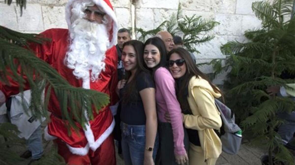 Israeli women pose for a picture with a Palestinian man dressed as Santa Claus standing between Christmas trees at a municipality distribution point at Jaffa Gate in Jerusalem&#039;s old city, ahead of Christmas celebrations.