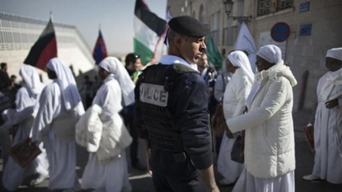 A Palestinian policeman stands guard as Nigerian worshippers cross a street near the Church of the Nativity in the Biblical West Bank city of Bethlehem, believed to be the birthplace of Jesus Christ, in the West Bank town of Bethlehem, as the Holy Land prepares to mark Christmas.