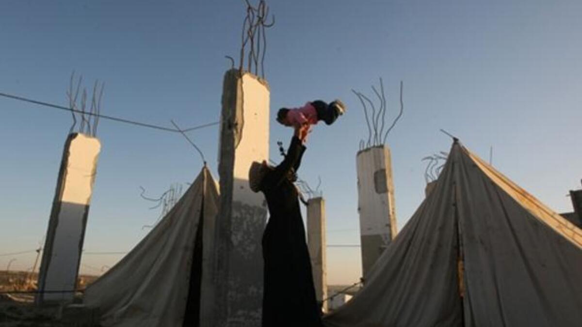 A displaced Palestinian woman carries her child outside their tent, in the Ezbet Abed Rabbo area, that was heavily destroyed during Israel's 22-day offensive on the Gaza Strip.